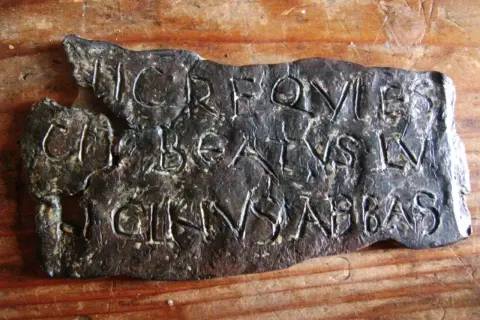 Plaque de métal gravée de lettres latines, possiblement une inscription trouvée près de la tour de Saint-Lupicin.
