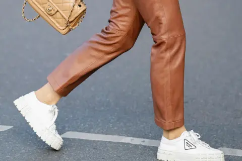 Un outfit chic con pantaloni in pelle marrone e sneakers bianche donna Prada. Una borsa Chanel completa il look.