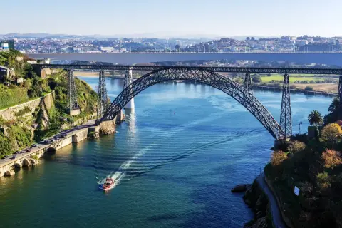 Majestatyczny porto most nad błękitną rzeką, z łodzią przecinającą fale i miastem w tle.