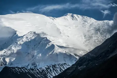 Majestatyczny pik Lenina w śnieżnej szacie, z ciemnymi, skalistymi zboczami w pierwszym planie i błękitnym niebem.