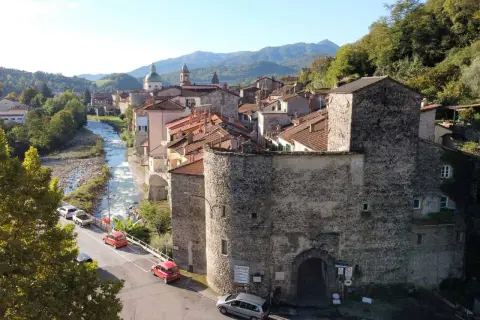 Antica porta in pietra lungo la via del Volto Santo, con fiume e case arroccate sui monti.