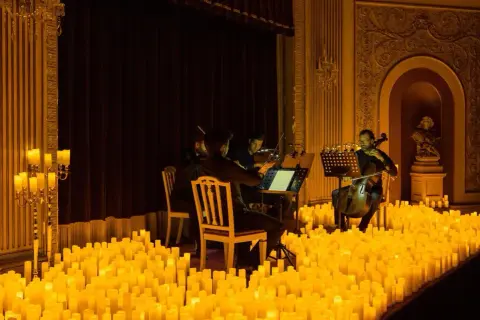 Un concierto de música clásica bajo la luz de miles de velas en Zaragoza. Músicos tocan violines y violonchelos en un escenario iluminado por velas.