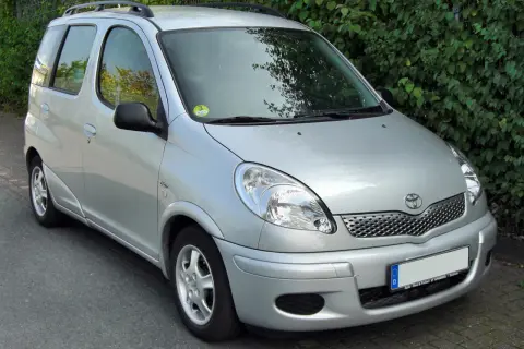 Srebrny Toyota Yaris Verso zaparkowany przy żywopłocie.