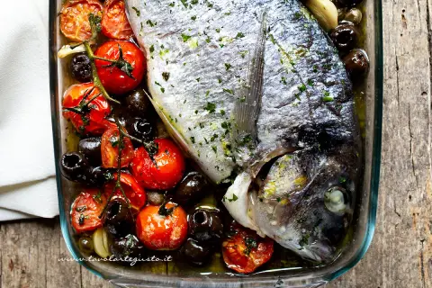 Orata al forno succulenta con pomodorini, olive nere e erbe aromatiche, pronta per essere gustata.