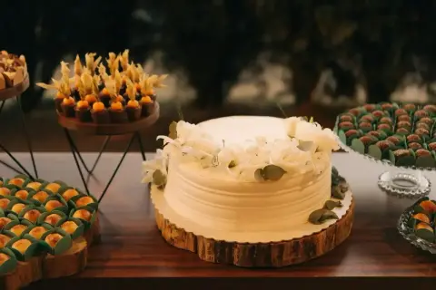 Biały tort komunijny ozdobiony białymi kwiatami i zielonymi listkami. Idealne jakie kwiaty na tort komunijny.