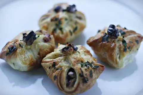 Cztery apetyczne paczuszki z ciasta francuskiego z gruszkami i gorgonzolą, posypane ziołami.