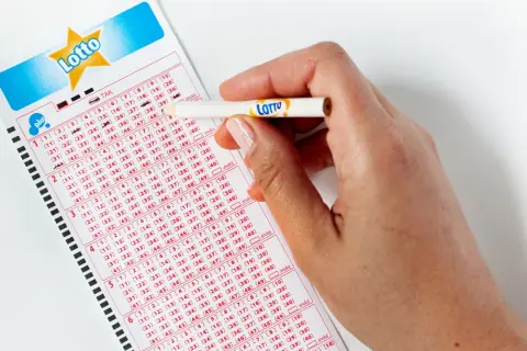Dłoń z ołówkiem zaznacza liczby na kuponie gry Lotto.