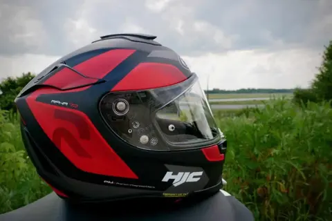 Czerwono-czarny kask motocyklowy HJC RPHA 70 z przyciemnianą blendą, gotowy na podróż pośród zieleni.