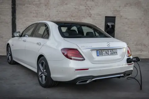 Un Mercedes 300de blanco, con el distintivo "E 300de", está enchufado a un cargador eléctrico.