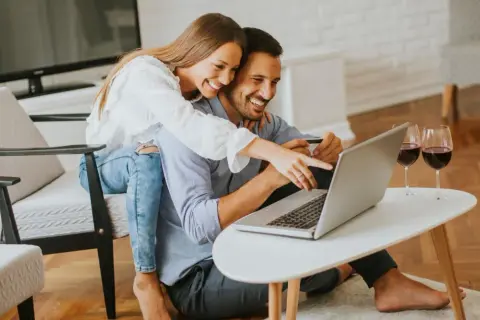 Szczęśliwa para robi zakupy online, ciesząc się ulgą na internet i lampką wina.