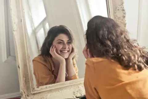 Donna sorride guardandosi allo specchio, un momento di riflessione sull'effetto specchio psicologia e sull'accettazione di sé.