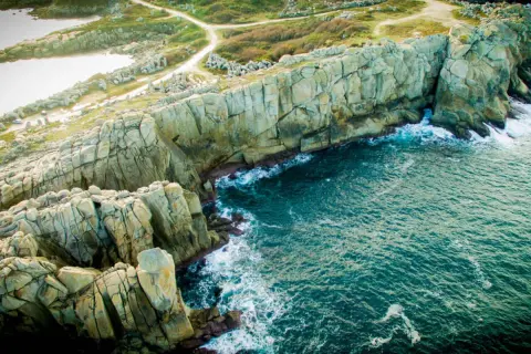 Impresionantes acantilados galicia, con el mar azul turquesa rompiendo contra las rocas. Senderos serpentean por la vegetación verde.