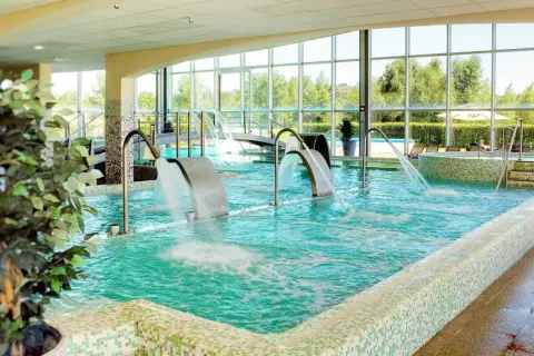 Piscina interior con cascadas de agua y vistas al exterior, ideal para una experiencia de spa relajante.