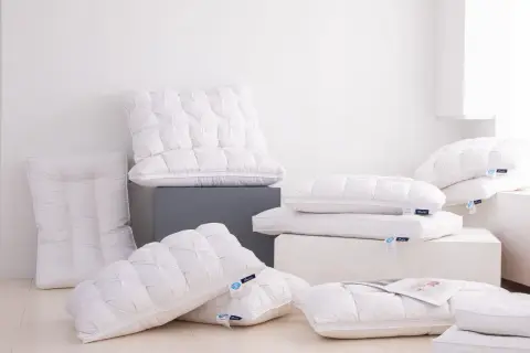 A pile of fluffy white down pillows, some with tufted patterns. One new down pillow smells bad, but the others look inviting.