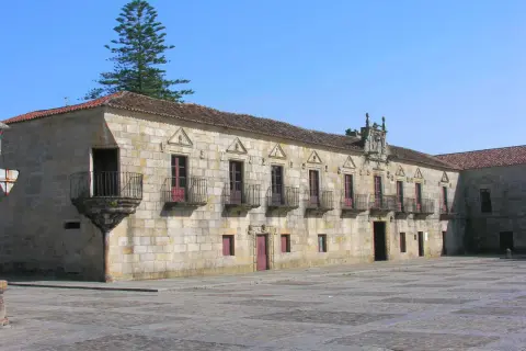 El Pazo de Fefiñanes, un edificio de piedra con balcones de hierro forjado, se alza bajo un cielo azul.