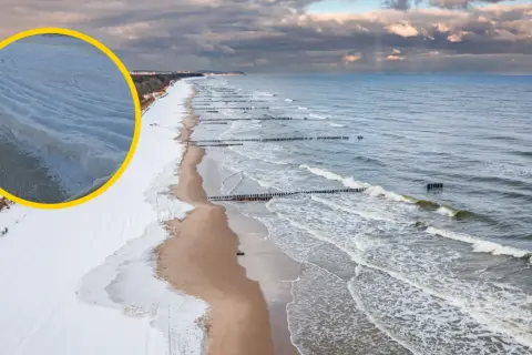 Zimowy Bałtyk z lodowymi falami przy brzegu. Czy bałtyk zamarzał? Widać zamarznięte przybrzeżne warstwy wody i śnieg na plaży.