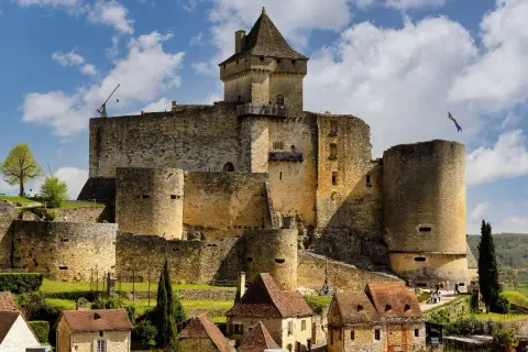 Un château médiéval impressionnant, l'un des célèbres châteaux en France, se dresse sur une colline verdoyante, sous un ciel bleu parsemé de nuages.