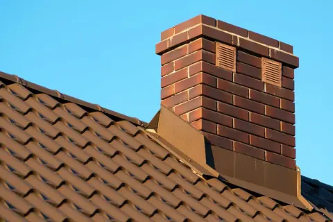 Ziegel-Schornstein auf braunem Ziegeldach vor blauem Himmel. Überlegungen, den alten Schornstein stilllegen zu lassen, sind im Gange.