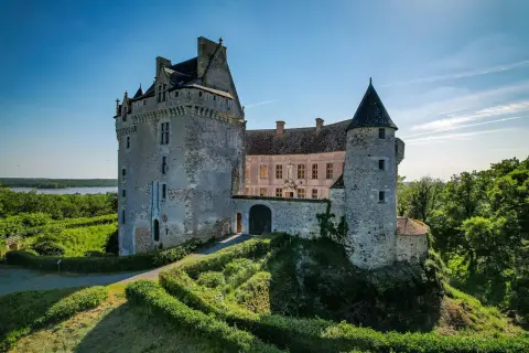 Le majestueux **château du Bouchet** se dresse fièrement sur une colline verdoyante, dominant un lac paisible sous un ciel bleu éclatant.