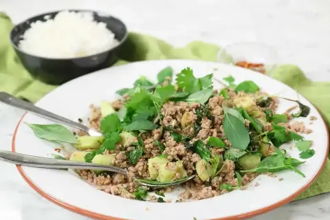 En tallrik med kycklingfärs, färska örter och grönsaker, perfekt för ett snabbt larb recept. Ris i bakgrunden.