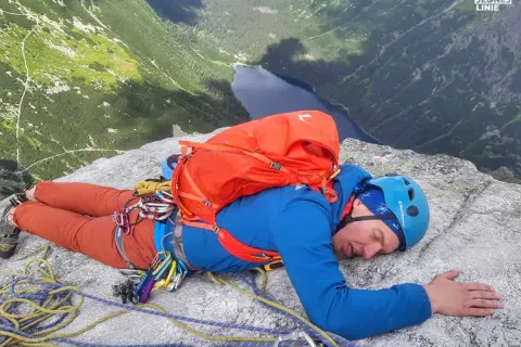 Zmęczony wspinacz odpoczywa na skale po wejściu na mnicha. Widok na jezioro i góry.