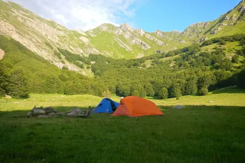Tende da campeggio in un prato verde, con montagne boscose sullo sfondo, vicino alle sorgenti del Secchia.