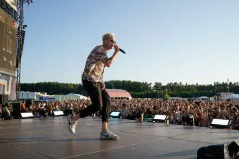 Wokalista One Republic na koncercie, śpiewa do mikrofonu na scenie przed rozentuzjazmowanym tłumem fanów.