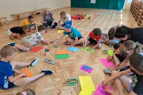 Dzieci klas 1-3 biorą udział w zabawach integracyjnych, rysując i kolorując na podłodze.