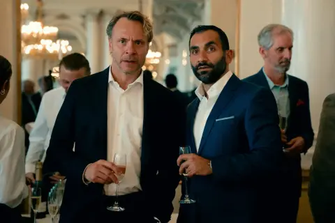 Två män i kostym med champagneglas i handen, en del av rollistan i Hundarna.