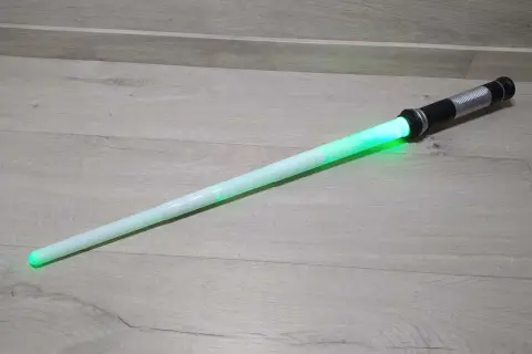 Zielony miecz Star Wars leży na drewnianej podłodze.