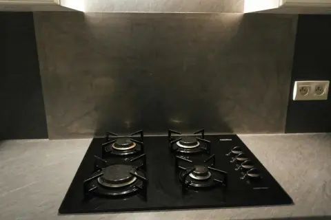 Plaque de cuisson noire avec quatre feux, devant un mur de crédence gris métallisé.
