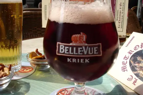 Szklanka piwa cherry Kriek Bellevue z pianką, obok jasne piwo i miseczki z przekąskami.
