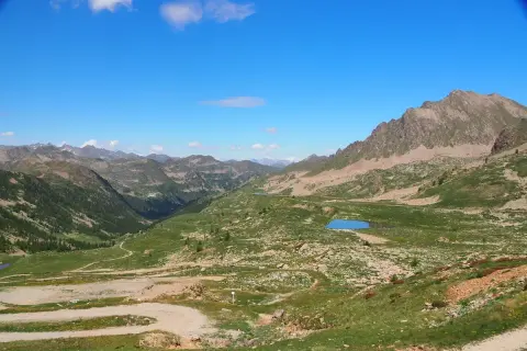 Vue panoramique du col de la Lombarde, avec des montagnes verdoyantes, des lacs bleus et un ciel clair.