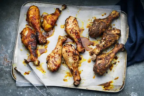 Nio saftiga kycklingben, vissa kryddade med chili, ligger på en plåt. Perfekt innertemp kycklingben för en härlig måltid.