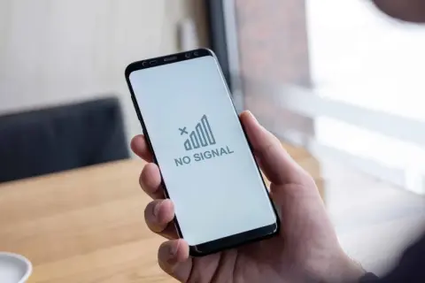 Dłoń trzyma smartfon z komunikatem "NO SIGNAL". Brak sieci w telefonie uniemożliwia kontakt.