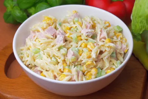 Pyszna sałatka z makaronem orzo, kukurydzą, szynką i selerem, polana kremowym sosem.