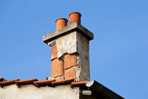 Zwei Ziegelrohre ragen aus einem alten, beschädigten Schornstein. Der **Schornstein nass unten** zeigt deutliche Verwitterungsspuren.