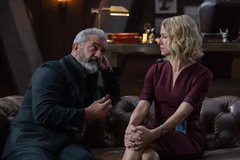 Mel Gibson w filmie, z cygarem w dłoni, rozmawia z kobietą w bordowej sukience.