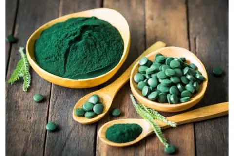Chlorella vs spirulina: zielony proszek i tabletki na drewnianym tle. Dwa rodzaje alg w formie suplementów diety.