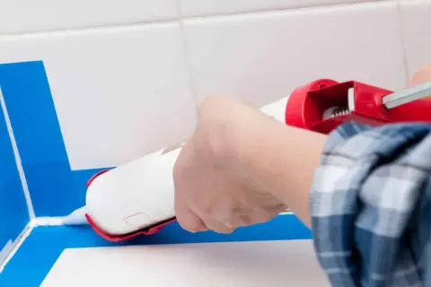Application d'un joint époxy pour douche, avec du ruban bleu pour un résultat net.