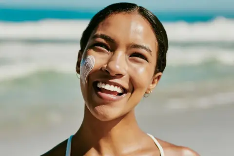 Strahlendes Lächeln am Strand, Sonnencreme schützt vor Hautalterung.