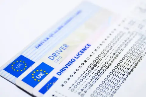Dwa brytyjskie prawa jazdy i wydruk z danymi.