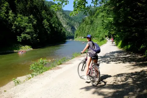 Dziewczyna na rowerze na malowniczej trasie rowerowej w Szczawnicy. W tle Dunajec z tratwami i zalesione góry.