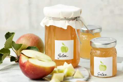 Zwei Gläser mit selbstgemachtem Apfelgelee, daneben frische Äpfel und gewürfelte Apfelstücke. Ein leckeres Apfelgelee Rezept zum Nachmachen.