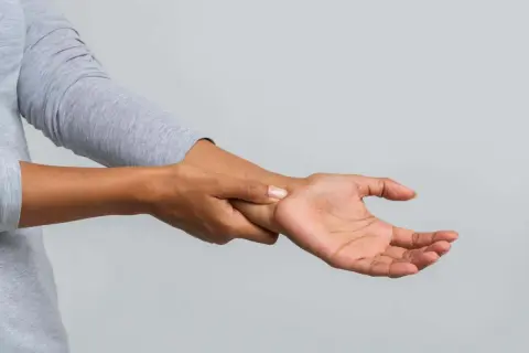 Eine Person hält sich das Handgelenk, als ob sie ein Ziehen im Handgelenk spürt.
