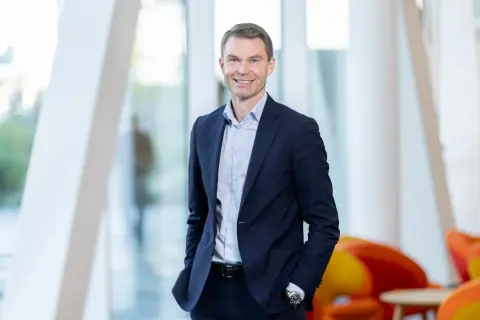 En leende man i mörkblå kostym, en del av Swedbank koncernledning, står framför ett modernt fönsterparti.