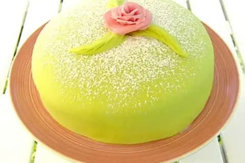 En vacker prinsesstårta med grön marsipan, pudrad med florsocker och dekorerad med en rosa ros. Perfekt för ett prinsesstårta recept!