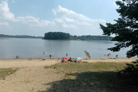 Słoneczny dzień nad jeziorem przeczyckim. Ludzie odpoczywają na plaży i kąpią się w wodzie.
