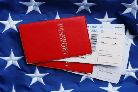 Czerwony paszport i bilety lotnicze na tle flagi USA. Zastanawiasz się, ile kosztuje bilet do USA w dwie strony?