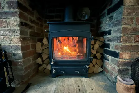 Poêle à bois allumé dans une cheminée en briques, avec du bois empilé. La **réglementation tubage poêle à bois** assure une évacuation sûre des fumées.